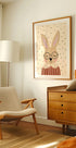 a cozy living room with a beige armchair, a wooden dresser, and a framed picture of a rabbit wearing glasses.