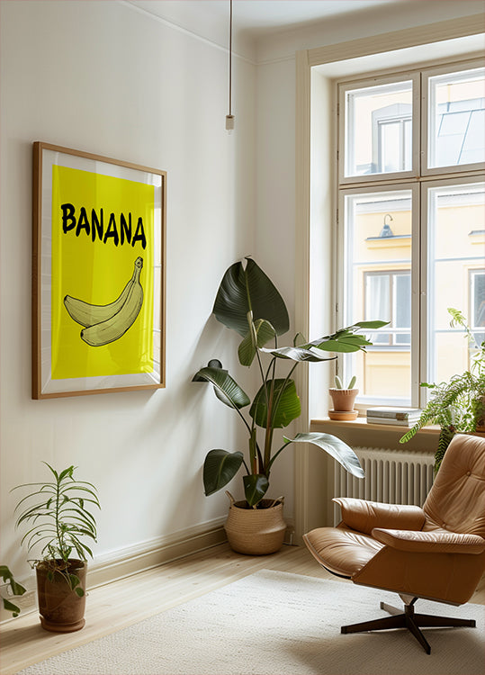 a cozy living room with a large window, a framed poster of a banana, a potted plant, and a comfortable armchair.